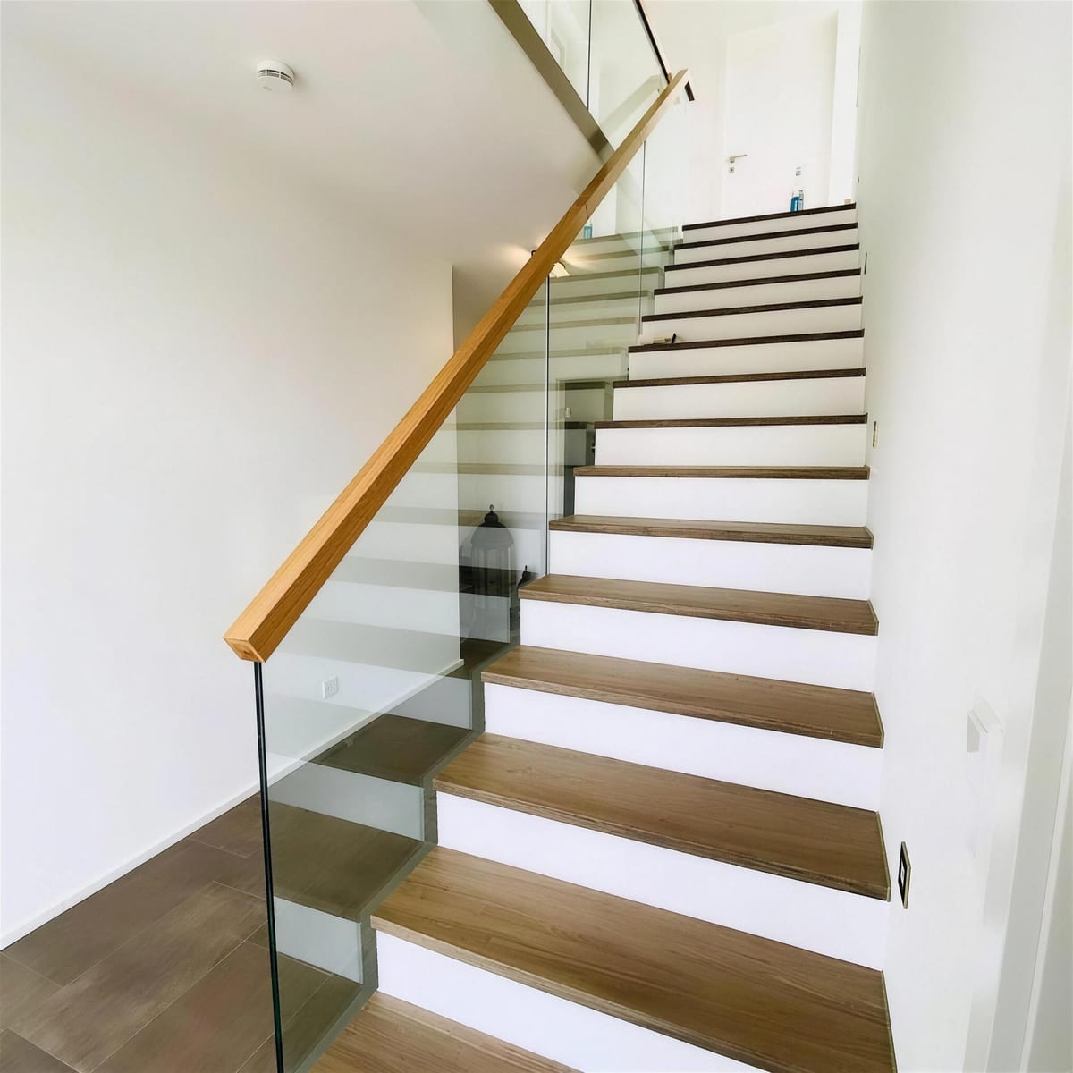 Ganzglasgeländer mit hölzernem Handlauf an einer offenen Treppe im Wohnhaus
