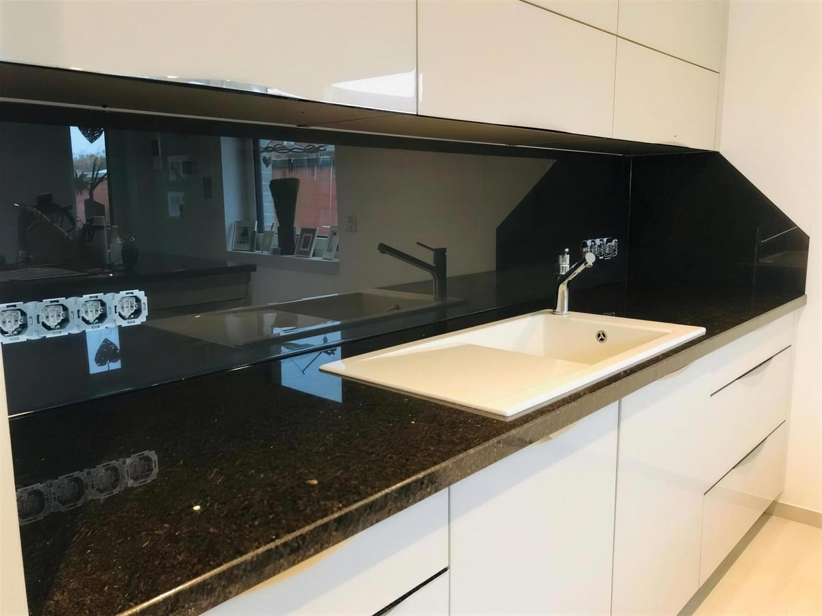 Schwarz lackierte Glasrückwand über einer Granitarbeitsplatte mit weißer Spüle