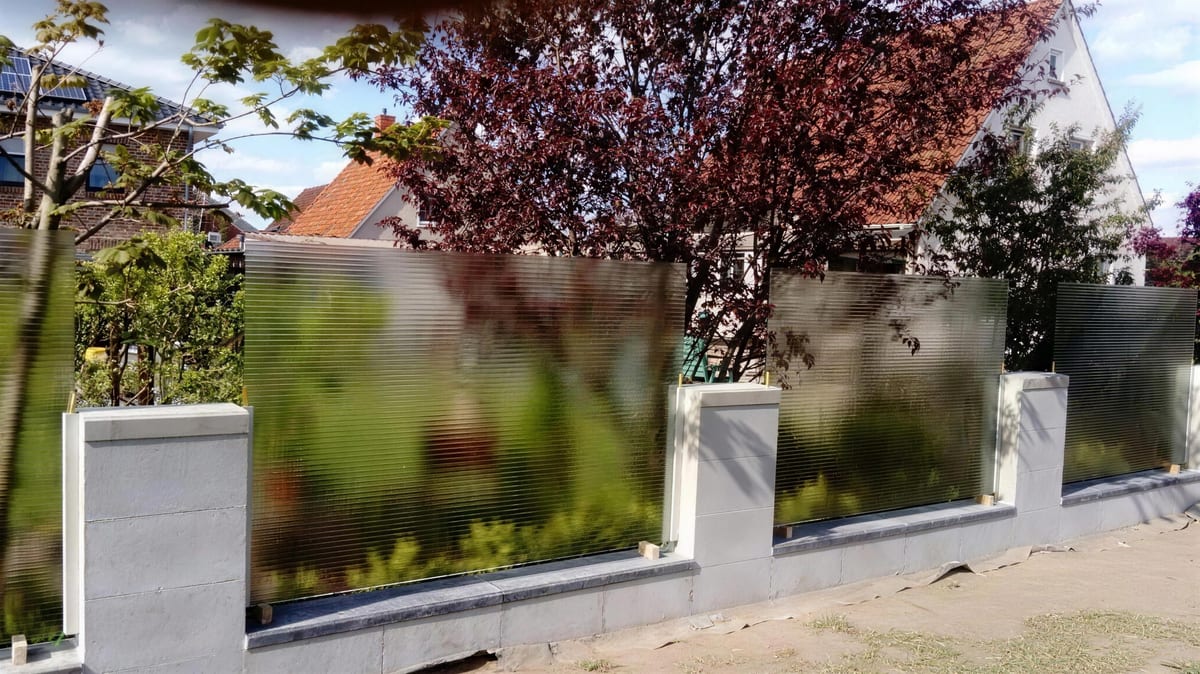Satinierte Glaswand als Sichtschutz auf einer Gartenmauer, dahinter Bäume