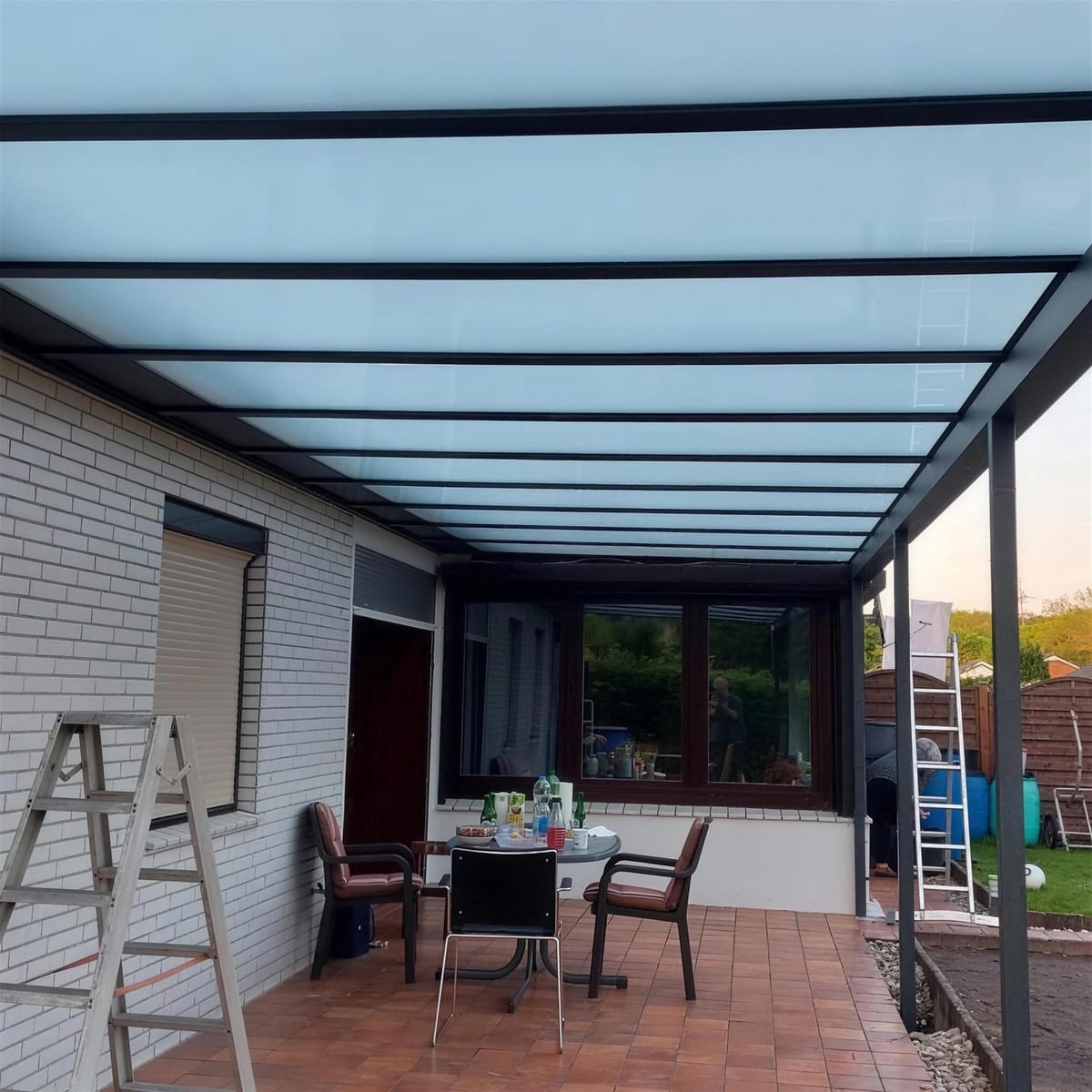 Fertige Terrassenüberdachung aus Glas mit Sitzgruppe darunter, abends