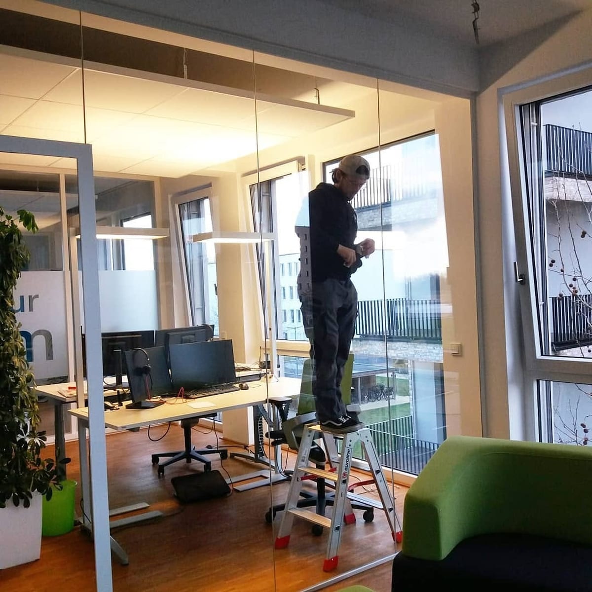 Monteur der Glaserei Honstein richtet auf einer Leiter eine Ganzglas-Trennwand im Büro aus
